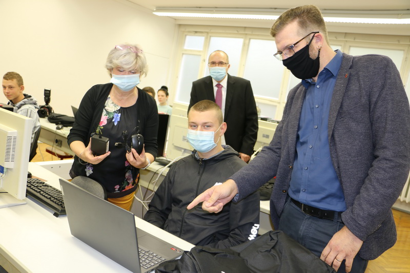 Bild vergrößern: Nick Grimm (rechts) zeigt Till Gerbig den neuen Laptop, Schulleiterin Simone Heilmann mit Maus und Ladekabel, dahinter Steffen Zenner.