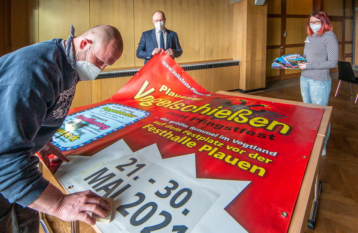 Bild vergrößern: Festhallen-Mitarbeiter Sebastian Opel bereitet die Werbeplane für das Plauener Vogelschießen vor. Unterstützt wird die Traditionsveranstaltung von Kultur- Bürgermeister Steffen Zenner und Eventmanagerin Anne Krieger (von Links).