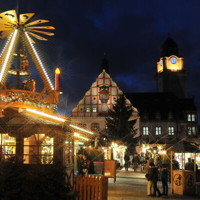 Bild vergrößern: zu sehen ist der Plauener Weihnachtsmarkt bei Nacht. Im Vordergrund dreht sich die die geschmückte Pyramide, Im Hintergrund ist das Alte Rathaus und der Beleuchtete Rathausturm zu sehen.