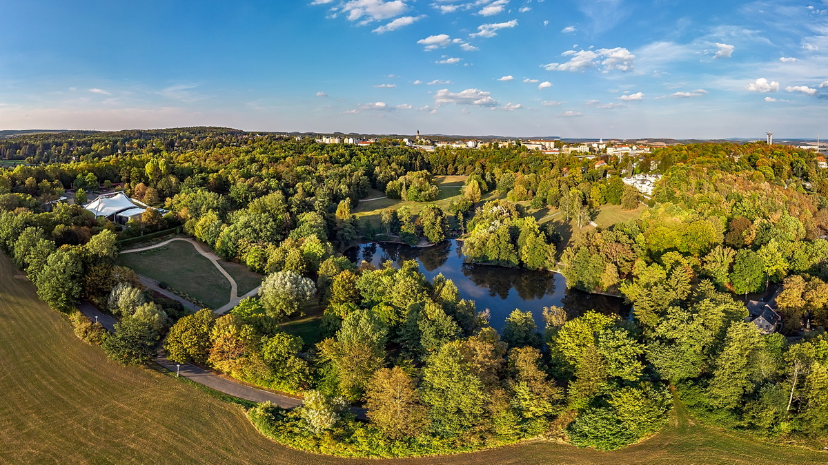 Bild vergrößern: Der Stadtpark aus der Vogelperspektive. Zu sehen ist der Teich und sein umliegender Wald.